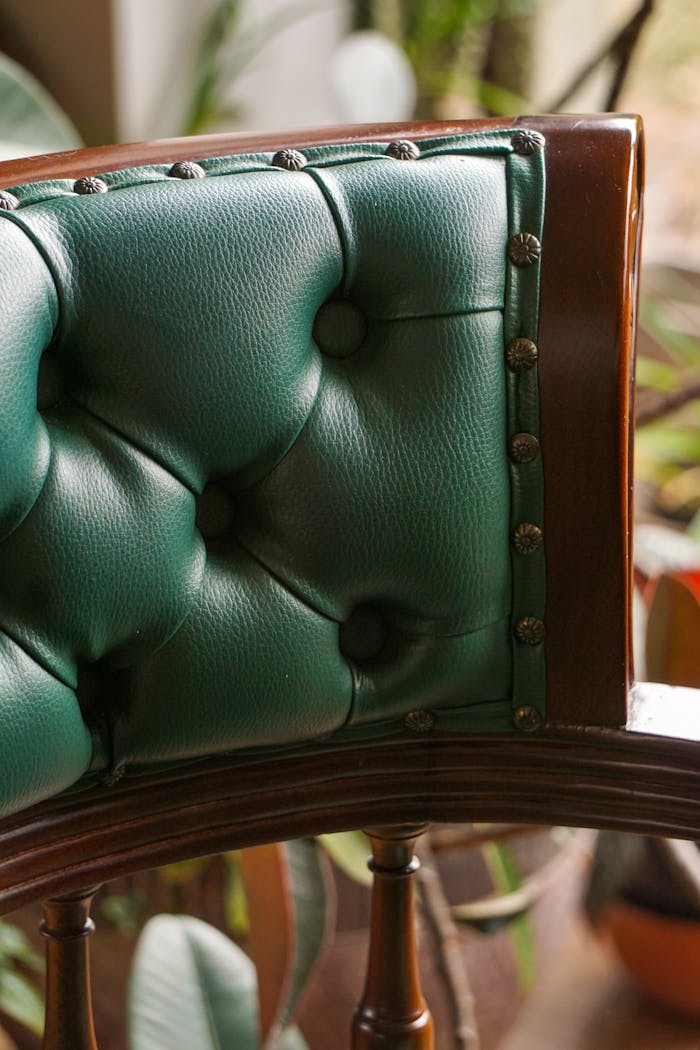 Close-up of a green leather and wooden chair, highlighting detailed upholstery.