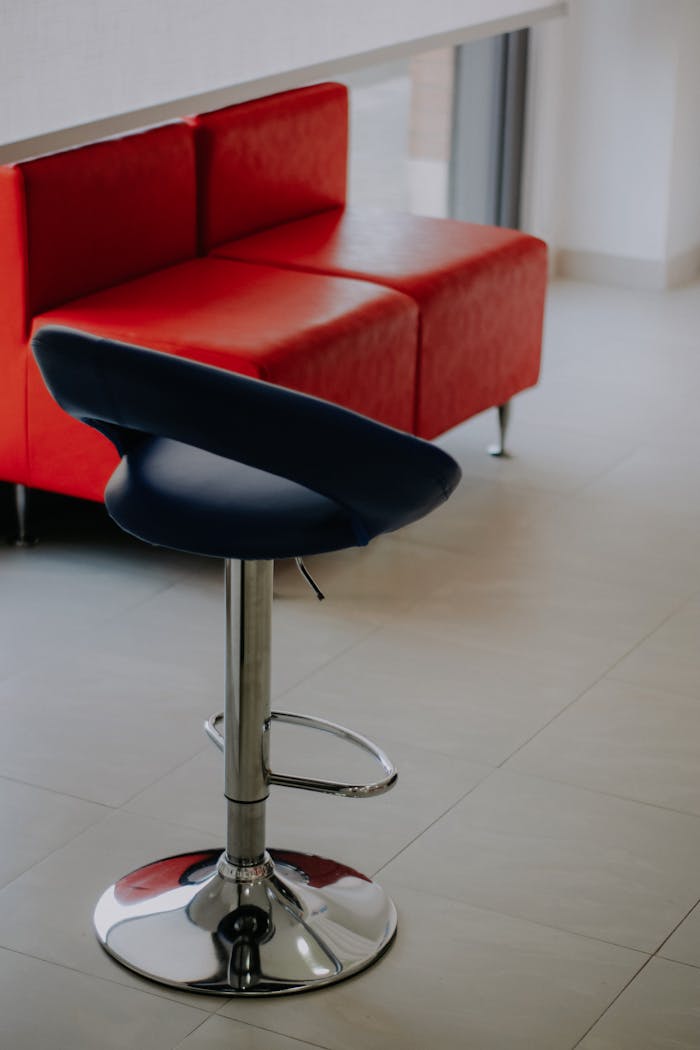 Contemporary interior with a sleek blue chair and vibrant red sofa on tiled floor.